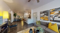 This single-story residence showcases a thoughtfully designed open-concept floor plan that seamlessly connects the living, dining, and kitchen areas into one cohesive, flowing space. Dark hardwood-style flooring runs throughout, providing a rich contrast against the bright white walls and ceilings. Ceiling fans are installed in multiple rooms, adding both function and style.

The living area is generously proportioned, featuring large windows that invite abundant natural light and views of surrounding greenery. The space accommodates a comfortable seating arrangement anchored by a natural wood slab coffee table and bold, contemporary artwork.

The kitchen is well-appointed with dark walnut cabinetry, granite countertops, stainless steel appliances, and a peninsula island with pendant lighting overhead—ideal for casual dining or meal preparation. The adjacent dining area provides additional seating space.

The bedroom is a tranquil retreat, featuring a ceiling fan, sliding glass door access to an outdoor area, and warm, layered décor. The bathroom offers a granite-topped vanity with dark wood cabinetry, a large mirror, and a full tub-shower combination with subway tile surround. Overall, the space delivers a modern, stylish aesthetic with practical, quality finishes throughout.