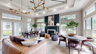 Located at 1623 Parkridge Cir in Crofton, Maryland, this single-floor community space offers a thoughtfully designed, open-concept layout that seamlessly blends comfort and contemporary style. The main gathering area commands attention with soaring tray ceilings adorned with a striking brass mid-century modern chandelier, adding a sculptural focal point overhead. Light hardwood flooring runs throughout, contributing to a warm and cohesive aesthetic.

The living and lounge area centers around a dramatic floor-to-ceiling dark navy shiplap fireplace wall with a classic white mantle and herringbone tile surround, serving as the room's architectural anchor. An abundance of oversized windows and glass doors flood the interior with natural light while offering views of the surrounding greenery.

The space accommodates multiple seating and dining arrangements, making it well-suited for both social gatherings and quiet retreats. A dedicated kitchen features bold navy cabinetry with gold hardware, a curved white quartz island with bar seating, a chevron-patterned tile backsplash, and glass-front upper cabinets — delivering both function and design sophistication. French doors provide additional access points, enhancing the flow between indoor and outdoor areas. Crown molding and recessed lighting complete the polished, upscale character of this well-appointed community space.