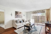 Located at 15513 Williams St in Tustin, CA, this single-story, one-bedroom, two-bathroom home offers a well-planned layout with hardwood flooring throughout the main living areas. The open-concept living room flows naturally into the dining area, with a ceiling fan overhead and a sliding glass door that opens to a private outdoor patio — ideal for bringing in natural light and fresh air. The kitchen features white cabinetry, a granite-style countertop with a breakfast bar peninsula, recessed lighting, and white appliances, including a range and refrigerator. The adjoining dining space comfortably accommodates a small table and is defined by its own pendant lighting. The spacious bedroom includes a ceiling fan with light fixture, carpeted flooring, a window with outdoor views, and direct access to a dedicated closet. The en-suite vanity area offers a wide mirror, white cabinetry, and hardwood flooring, with natural light from a side window. The second full bathroom features a tub/shower combination and a decorative mirror. A textured ceiling is found throughout. The private patio, accessible from the living room, provides an outdoor seating area with surrounding greenery, completing this efficiently designed home.
