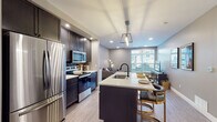 Located at 50 S Grant Ave in the heart of Columbus, Ohio, this stylish single-floor residence offers a thoughtfully designed open layout with contemporary finishes and abundant natural light. The kitchen is a standout feature, showcasing dark cabinetry, stainless steel appliances including a French door refrigerator, microwave, and range, all complemented by a spacious island with a white quartz countertop, undermount sink, and seating — illuminated by geometric pendant lighting. Light wood-style flooring flows throughout, creating a cohesive and modern aesthetic. The kitchen opens seamlessly into the living area, which is bathed in natural light from large windows and features recessed lighting and a cozy, well-proportioned layout. A separate sitting nook provides additional flexible living space. The two bedrooms are generously sized, each offering large windows with exterior views, soft neutral wall tones, and warm hardwood-style flooring. The bathroom is finished with large-format tile flooring, a white vanity with ample storage, a framed mirror, and matte black fixtures. Throughout the space, neutral gray tones, clean lines, and modern lighting choices contribute to a polished and inviting urban atmosphere ideal for contemporary living.