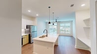 This well-appointed one-bedroom, one-bathroom unit in Opelika, Alabama offers a thoughtfully designed open-concept layout with modern finishes throughout. The combined kitchen and living area serves as the heart of the home, anchored by a striking white quartz island with an undermount sink and matte black faucet. The kitchen features white upper cabinetry, warm wood-toned lower cabinets, a subway tile backsplash, stainless steel appliances including a refrigerator and microwave, and stylish pendant lighting. Hardwood-style flooring flows throughout the main living areas, adding warmth and continuity. The spacious living room is flooded with natural light from large windows and a glass sliding door, complemented by a ceiling fan overhead. Built-in shelving adds a functional architectural detail to the living space. The bedroom is generously sized, finished with plush carpet, a ceiling fan, and large windows that invite natural light. Three closets provide ample storage throughout the unit. The full bathroom is elegantly appointed with a wood-toned vanity, white quartz countertop, undermount sink, matte black fixtures, subway-tiled tub surround, and wood-look flooring. A dedicated laundry area and pantry round out this efficient and modern floor plan.