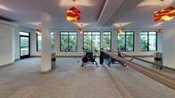 Located at 323 Seven Springs Way in Brentwood/Nashville, TN, this amenity floor offers a well-appointed collection of shared spaces designed for both productivity and leisure. Wide, carpeted corridors adorned with framed black-and-white photography connect the various areas, creating a polished and welcoming atmosphere throughout.

The social lounge serves as a central gathering space, featuring a fireplace, large-format wall-mounted television, colorful abstract artwork, and a mix of seating including plush armchairs, sofas, and small café-style tables. Pendant lighting and recessed fixtures contribute to a warm, inviting ambiance. A glass-railed overlook adds an architectural focal point to the lounge area, with rows of windows bringing in natural light.

A dedicated conference room provides a professional meeting environment, equipped with a substantial wood conference table, ergonomic task chairs, a wall-mounted display screen, and a striking geometric chandelier. Natural light enters through a window with exterior views.

The billiards room offers a leisure-focused retreat, centered around a full-size pool table beneath modern pendant lighting, with music-themed framed artwork decorating the walls.

A kitchenette with dark cabinetry, granite countertops, a mosaic tile backsplash, and stainless steel appliances supports the amenity spaces. Additionally, a fitness or activity area with vibrant pendant lighting and digital display screens rounds out the floor's offerings.