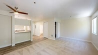 Located at 9300 W Mall Dr in Everett, Washington, this efficiently designed single-floor unit offers a well-organized layout comprising a living room, kitchen, bathroom, and closet. The living area features a ceiling fan, warm neutral-toned carpet, and a sliding glass door that opens to a private balcony overlooking lush, mature greenery — bringing in natural light and a serene outdoor connection. A structural column subtly defines the boundary between the living space and the kitchen pass-through, which features a raised breakfast bar counter with granite-style laminate surfaces. The galley-style kitchen is thoughtfully arranged with white cabinetry along both walls, granite-style countertops, white appliances including an electric range and refrigerator, and light hardwood-style flooring that runs throughout the kitchen and entry areas. A dedicated closet provides convenient storage, while the full bathroom includes a soaking tub and shower combination, toilet, and matching granite-style vanity countertop. The unit's light beige walls and neutral palette throughout create a clean, cohesive ambiance, making this a practical and comfortable space in Everett's Westside area.