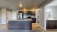Located at 331 Cedar Bird Ln in Holmen, Wisconsin, this single-floor home offers a thoughtfully designed layout with modern finishes throughout. The open-concept living and kitchen area serves as the heart of the home, where warm hardwood-style flooring transitions seamlessly into plush carpeting in the living space. Recessed lighting illuminates the area, creating a bright and welcoming atmosphere.

The kitchen is well-appointed with dark espresso cabinetry, granite countertops, and a full suite of stainless steel appliances, including a French door refrigerator, electric range, and built-in microwave. A sizeable kitchen island with a sink and matching granite surface provides additional workspace and casual seating potential, anchoring the open layout.

The bedrooms feature neutral carpet flooring and are generously equipped with storage, including dual closets fitted with wire shelving systems. The bathroom includes dark cabinetry with a white countertop vanity, wood-look vinyl flooring, and matte black hardware accents for a contemporary feel.

A dedicated laundry area accommodates a stacked washer and dryer unit alongside built-in wire shelving for added storage convenience. Baseboard heating is present throughout, and the overall color palette of soft grays and warm neutrals lends the home a clean, modern aesthetic.