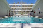 Located at 4387 Sibley Bay St in Punta Gorda, Florida, this single-story outdoor pool facility offers a well-appointed aquatic space designed for both recreation and lap swimming. The centerpiece is a generously sized rectangular pool with clear, blue-green water, marked lane dividers, and clearly posted depth indicators — making it suitable for structured swim sessions as well as leisure use.

The pool is fully enclosed within a white-framed screen enclosure, featuring a sloped, transparent roof that allows abundant natural sunlight to flood the space while providing protection from insects and debris. The enclosure opens up to views of the surrounding mature tree canopy, lending the space a natural, serene ambiance characteristic of Southwest Florida.

The surrounding pool deck is finished in a smooth, light-colored surface and offers ample room for lounging and outdoor furniture. Seating arrangements, including chairs and a table, are positioned along the perimeter, providing comfortable spaces to relax. Safety equipment, including a life ring, is visibly mounted on the wall. A raised deck section along one side extends the usable outdoor space, offering additional seating and views of the greenery beyond the enclosure. The overall setting is bright, open, and well-maintained, reflecting the relaxed Florida lifestyle.