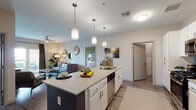 This single-floor residence features a thoughtfully designed open-concept layout connecting the kitchen, dining, and living areas. The kitchen is a standout, centered around a large island with a light quartz countertop, an undermount sink, and bar seating for several guests. Pendant lighting hangs above the island, complementing the white cabinetry, stainless steel appliances—including a gas range, built-in microwave, and French door refrigerator—and wood-style flooring that extends throughout the common areas.

The living room offers a welcoming atmosphere with vaulted ceilings, a ceiling fan, and French doors leading to a private outdoor balcony. Natural light filters in through the glass doors, enhancing the open feel of the space.

The two bedrooms are carpeted and well-proportioned, each with windows that allow natural light. The primary bedroom is particularly spacious, accommodating a large bed and seating area. The primary bathroom features a double-sink vanity with white cabinetry, a glass-enclosed walk-in shower, and wood-style tile flooring. A secondary bathroom offers a tub-shower combination with white tile surround and neutral finishes throughout.