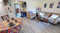 This single-floor unit at 3800 14th Ave SE in Lacey, Washington offers a well-organized and functional layout designed for comfortable everyday living. The living area features light wood-look flooring, a textured ceiling, and a large window with vertical blinds that invites natural light into the space. A baseboard heater provides warmth, and the room comfortably accommodates a full seating arrangement alongside a dining area. The galley-style kitchen is efficiently designed with dark cabinetry lining both walls, providing ample storage. It is equipped with a white electric range, a full-size refrigerator, and a stainless steel sink set into a laminate countertop. A doorway from the kitchen leads directly into the bedroom, enhancing the flow of the unit. The bedroom is carpeted and features a textured ceiling, a window that allows natural light in, and two sets of dark sliding closet doors offering generous storage space. An en-suite bathroom is accessible directly from the bedroom, adding convenience and privacy. Throughout the unit, the color palette remains light and neutral, contributing to a bright and welcoming atmosphere. The combination of practical finishes and a connected layout makes this a highly functional Lacey residence.