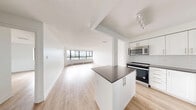 Located at 545-565 Belmont Ave W in Kitchener, Ontario, this well-appointed one-bedroom, one-bathroom unit offers a clean, modern aesthetic throughout. Light hardwood-style flooring runs continuously across the space, complementing the crisp white walls and creating a bright, cohesive feel.

The open-concept living room and kitchen area is a standout feature, anchored by expansive floor-to-ceiling windows that frame impressive views of the Kitchener skyline and flood the space with natural light. The kitchen is thoughtfully designed with white shaker-style cabinetry, grey countertops, a white subway tile backsplash, and stainless steel appliances including a range, over-the-range microwave, and dishwasher. A peninsula with a dark countertop provides additional prep and casual dining space.

The bedroom is a comfortable size, featuring a window with city views, a baseboard heater, and a mirrored sliding-door closet that enhances the sense of space and light. A dedicated closet offers additional storage.

The bathroom is finished with grey rectangular wall tiles surrounding a full soaker tub and shower, complemented by tile flooring, a white vanity, and a mirrored medicine cabinet. The overall ambiance of the unit is clean, contemporary, and move-in ready.