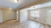 Located at 4676 Albany Post Rd in Hyde Park, NY, this single-floor 1-bedroom, 1-bathroom unit offers a thoughtfully updated interior with a clean, modern aesthetic throughout. Light wood-look flooring flows seamlessly across the main living area, which features neutral warm-toned walls, baseboard heating, and a wall-mounted AC unit. A large window frames views of the surrounding wooded landscape, filling the space with natural light. The open layout connects the living area to the kitchen, which stands out with crisp white shaker-style cabinetry, quartz countertops with subtle veining, and a striking herringbone wood-pattern tile backsplash. A window above the counter continues the theme of natural light and outdoor views. The bedroom is a comfortable, well-proportioned room with wood-look flooring, a window overlooking the trees, a baseboard heater, and a closet with built-in shelving. The bathroom is finished with large-format dark tile flooring, neutral gray walls, and a tub/shower combo featuring elegant marble-style surround panels and chrome fixtures. A window provides natural ventilation. The unit presents a well-maintained, move-in-ready residence in the scenic Hudson Valley.