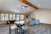 Located at Decatur Plaza in Omaha, Nebraska, this single-floor community clubhouse offers a thoughtfully designed layout that blends comfort and functionality. The open-concept living room impresses with soaring vaulted ceilings accented by exposed wood beams, plush carpeting, and a tile-surround fireplace with a built-in entertainment niche — creating a warm, welcoming gathering space. Large windows allow natural light to fill the room, enhancing the relaxed ambiance.

The adjacent dining area features tile flooring, a chandelier overhead, and ample space for group seating around a central round table. Tasteful wall art and neutral tones give the room a clean, modern feel. The kitchen is well-equipped with warm oak cabinetry, tile backsplash, stainless steel appliances including a full-size refrigerator, and a breakfast bar with stylish swivel bar stools — ideal for casual dining or socializing.

The dedicated exercise room provides a practical fitness space outfitted with cardio equipment, a full rack of dumbbells, a wall-mounted television, and access to restroom facilities. A door connects directly to the outdoor pool area, which features lounge seating and a resort-style pool, extending the recreational amenities of this versatile community space.