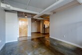 Located at 127 W Tenth Street in Kansas City, MO, this urban loft-style unit showcases an industrial-modern aesthetic throughout. The open living areas are anchored by polished concrete floors that reflect light and lend a sleek, contemporary feel, while exposed ductwork and pendant lighting suspended from the ceiling reinforce the loft-inspired character of the space.

The galley kitchen is well-appointed with white cabinetry, dark countertops, stainless steel appliances including a refrigerator, electric range, and dishwasher, as well as track lighting overhead and the same concrete flooring that flows through the main living areas.

A dedicated laundry area houses a side-by-side Bosch washer and dryer, offering a convenient in-unit amenity. The bedroom features warm carpeting and a window that draws in natural light, creating a comfortable contrast to the harder surfaces found elsewhere. A staircase with dark wood railings leads to a secondary area, flanked by windows that provide additional natural light and views of the surrounding urban streetscape.

The bathroom includes a tub-shower combination, a vanity with a light wood finish, built-in shelving, and speckled flooring. Throughout the unit, a neutral gray and white color palette ties together the industrial and residential elements cohesively.