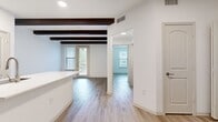 This 650-square-foot one-bedroom, one-bathroom apartment at Cool Springs offers a well-designed single-floor layout encompassing a combined kitchen and living room, one bedroom, one bathroom, and a dedicated closet. The living area is distinguished by striking exposed dark wood beam ceilings and light hardwood-style flooring that flows throughout, creating a warm yet contemporary aesthetic. Large windows fitted with horizontal blinds invite abundant natural light, while a glass patio door provides direct outdoor access and additional views. The kitchen is a functional centerpiece, featuring rich dark cherry wood cabinetry, a large white quartz island with an integrated sink, and a full suite of stainless steel appliances including a refrigerator, range, and microwave. The 170-square-foot primary bedroom offers a ceiling fan, a bright window with outdoor views, and direct access to a spacious walk-in closet with built-in shelving. The bathroom includes a full soaking tub and shower combination with neutral tile surround and chrome fixtures, complementing the unit's clean, understated palette of whites and warm wood tones throughout.