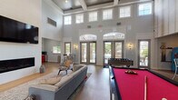 Located at 3101 Compatible Way in Raleigh, NC, this single-story community clubhouse combines striking architectural design with a broad range of amenities. The centerpiece is a soaring great room with dramatic coffered ceilings and an abundance of clerestory windows that flood the space with natural light. French doors along the back wall open to an outdoor pool area, seamlessly blending indoor and outdoor living. The game lounge is anchored by a vivid red billiard table and a foosball table, complemented by comfortable lounge seating and a bar-height counter adorned with colorful abstract artwork. A dedicated business center provides multiple computer workstations set on patterned carpet, enclosed by glass-paneled French doors for a semi-private work environment. Cozy nooks throughout the clubhouse offer intimate seating options, including a tufted leather sofa positioned beneath a large picture window overlooking lush greenery, and a private alcove with bold red accent chairs. The kitchenette features vivid red cabinetry, a sleek tile backsplash, open shelving, and compact appliances, providing a convenient refreshment station. Warm hardwood-style flooring, soft neutral tones, and curated modern furnishings contribute to a polished yet welcoming ambiance throughout.