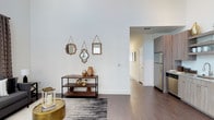 This two-story, 2-bedroom, 2-bathroom townhome offers a well-designed layout across two levels, combining modern aesthetics with functional living spaces. The interior showcases striking soaring ceilings that lend an airy, expansive feel to the main living area, complemented by rich hardwood-style flooring that flows seamlessly throughout. Clean white walls and thoughtfully placed décor accents create a bright, welcoming ambiance. The open-concept design connects the living area to the kitchen, which is equipped with stainless steel appliances, including a full-size refrigerator, and features warm wood-toned cabinetry. The layout provides a natural sense of flow between spaces, making the home ideal for both everyday living and entertaining. Outside, the townhome boasts a generously sized private backyard enclosed by a full-height wooden privacy fence, offering a secluded outdoor retreat with a well-maintained green lawn and a young shade tree. The exterior of the building presents a contemporary board-and-batten siding design in a neutral gray palette, contributing to its modern curb appeal. With a dedicated HVAC unit and multiple windows allowing natural light to filter in, this townhome blends comfort, style, and practicality in a cohesive package.