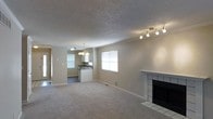 This two-floor residence offers a welcoming and functional layout designed for comfortable everyday living. The main living area is spacious and open, featuring neutral-toned carpet flooring, a textured ceiling, and a tiled fireplace with a classic white surround that serves as a natural focal point. A track lighting fixture overhead provides versatile illumination throughout the space, while a window allows natural light to fill the room. The living area flows seamlessly into the kitchen, which is outfitted with white cabinetry, a dark countertop, and a peninsula-style breakfast bar that defines the transition between spaces. An elegant chandelier hangs above, adding a touch of warmth to the kitchen area. A window above the sink brings in additional natural light, contributing to the bright and airy feel of the open-plan layout. The neutral color palette throughout creates a clean, move-in-ready aesthetic that offers flexibility for a variety of interior styles. With two floors, the home provides ample space for living, entertaining, and private retreats, making it a well-rounded and practical residence.