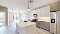 Located at 123 E Corporate Pl in Chandler, AZ, this well-designed one-bedroom, one-bathroom unit offers a thoughtful layout across a single floor. The open-concept living and kitchen area is anchored by a generous island with a sleek quartz countertop, an undermount sink, and a professional-style pull-down faucet. The kitchen features two-tone cabinetry — crisp white upper cabinets paired with gray lower cabinets — complemented by stainless steel appliances including a gas range, microwave, and dishwasher. Pendant lighting and recessed fixtures illuminate the space, while light wood-style flooring flows throughout the main living areas. The living room receives abundant natural light through a large sliding glass door that opens onto a private balcony, offering views of the surrounding community. The bedroom is carpeted for comfort and includes a ceiling fan and a sizable window that brings in additional natural light. A dedicated walk-in closet provides ample storage with multiple hanging rods and shelving. The bathroom is finished with light wood-look flooring, a gray vanity with an illuminated mirror, and a tiled soaking tub and shower combination.