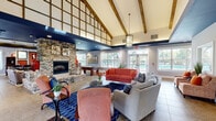Located at 801 E Brannon Rd in Nicholasville, KY, this single-story clubhouse for The Avenue Nicholasville is a well-appointed community gathering space offering a welcoming blend of rustic and contemporary design elements. The entrance greets visitors with a bold navy-accented ceiling, large-format tile flooring, and a branded welcome mat, setting the tone for the stylish interior beyond.

The main lounge area is the architectural centerpiece, featuring dramatically vaulted ceilings adorned with exposed wooden beams and decorative timber lattice panels. A floor-to-ceiling stacked stone fireplace anchors one end of the room, while comfortable seating arrangements — including coral-toned sofas and neutral sectionals — create an inviting social atmosphere. A statement pendant light fixture and recessed lighting complement the natural light that flows in from multiple windows.

A dedicated game area includes a billiard table positioned alongside large windows offering direct views of the outdoor pool. Adjacent seating nooks with patterned accent chairs provide quieter areas for relaxation or conversation. A dining area with dark wood tables and chairs also overlooks the pool through wide, light-filtering windows framed by a deep navy ceiling detail. Throughout the space, tile flooring, neutral gray walls, and carefully placed greenery contribute to a cohesive, polished aesthetic suitable for community events and everyday use.