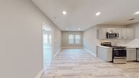 Located at 1207 E Armour Blvd in Kansas City, Missouri, this thoughtfully renovated apartment on the second floor offers a clean, contemporary aesthetic throughout its single-level layout. Light wood-tone luxury flooring runs seamlessly across the entire unit, creating a bright and cohesive feel in every room. The open living and dining area is bathed in natural light from multiple windows fitted with white horizontal blinds, complemented by recessed lighting that illuminates the neutral gray walls and crisp white trim. The kitchen is efficiently designed and features stainless steel appliances including a range, over-the-range microwave, and dishwasher, paired with gray shaker-style cabinetry, white quartz countertops, and a classic white subway tile backsplash. The bedroom is a comfortable, well-lit retreat with dual windows and a ceiling fan with integrated lighting. The bathroom is a standout space, showcasing marble-patterned tile on both the floor and tub surround, a stainless steel towel bar, and gray vanity cabinetry with a white countertop. A spacious entryway area provides access to multiple interior doors and benefits from its own recessed lighting, offering both functionality and a welcoming first impression.
