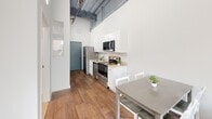 Located on the fourth floor at 601 Penn St in downtown Reading, PA, this 2-bedroom, 1-bathroom unit offers a thoughtfully designed layout that maximizes every square foot. The open kitchen and dining area immediately impresses with its dramatically high ceilings accented by exposed industrial beams, creating a loft-like ambiance. The kitchen is outfitted with stainless steel appliances—including a refrigerator, dishwasher, range, and over-the-range microwave—complemented by white cabinetry, light countertops, and rich hardwood flooring that flows throughout the unit. Both bedrooms are bright and efficiently sized, featuring large sliding windows that frame views of the surrounding downtown Reading cityscape, filling each room with natural light. The primary bedroom connects conveniently to the main living and kitchen area, while the second bedroom includes a double-door closet for added storage. The full bathroom is clean and functional, featuring a tub/shower combo, marble-style tile flooring, and neutral wall tones. Throughout the unit, crisp white walls and high ceilings contribute to an airy, open feel that belies its compact footprint. A distinctive blue entry door adds a modern design touch at the entrance.