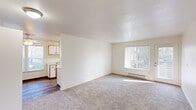 Located at 4505 SW Masters Loop in Beaverton, Oregon, this two-bedroom, one-bathroom residence offers a practical and well-organized single-floor layout. The living area features plush carpeting and a large window fitted with vertical blinds, allowing natural light to fill the space. A baseboard heating system runs along the exterior walls, ensuring year-round comfort. Adjacent to the living area, the galley-style kitchen is efficiently designed with ample white cabinetry, wood-toned trim accents, a stainless steel sink, white appliances including an electric range and refrigerator, and wood-look vinyl flooring. A window at the end of the kitchen provides additional natural light. A dining nook off the kitchen features a ceiling fan and windows with vertical blinds. The spacious primary bedroom offers generous square footage, carpeted flooring, a large window, and a built-in closet with shelving. The second bedroom also includes carpet and built-in shelving for convenient storage. The full bathroom is finished with wood-look flooring and includes a full tub-shower combination. A dedicated laundry area with a water heater and closet rod completes this functional and comfortable home.