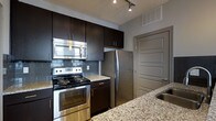 Located at 720 Michigan Ave in Columbus, Ohio, this single-floor residence offers a contemporary living experience with thoughtfully designed interiors. The kitchen is a standout feature, showcasing rich dark espresso cabinetry that extends to the ceiling for ample storage, complemented by granite countertops with subtle veining. A full suite of stainless steel appliances — including a range with electric cooktop, over-the-range microwave, and a full-size refrigerator — delivers both style and functionality. A grey subway tile backsplash adds a modern, textural element that ties the kitchen's aesthetic together cohesively. Track lighting illuminates the workspace efficiently, highlighting the clean lines and finishes throughout. The neutral grey walls provide a versatile backdrop that enhances the overall modern palette of the space. The layout flows naturally, with a well-defined kitchen area that connects to the rest of the unit. The attention to detail in the finishes — from the brushed hardware on the cabinetry to the undermount sink — reflects a commitment to quality and contemporary design throughout this well-appointed Columbus residence.