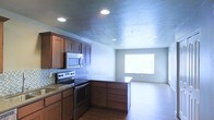 This single-floor space showcases an open-concept layout that seamlessly connects the kitchen and living area, creating a functional and cohesive environment. The kitchen is well-appointed with rich, warm-toned wood cabinetry offering generous storage, complemented by dark countertops and a subtle tile backsplash that adds texture and visual interest. Stainless steel appliances, including an electric range and over-the-range microwave, provide a modern touch. A kitchen peninsula extends into the space, offering additional workspace and serving as a natural divider between the kitchen and the adjoining living area. Recessed lighting is installed throughout the textured ceiling, ensuring consistent, even illumination across both zones. The living area features durable hardwood-style flooring that flows seamlessly from the kitchen, while a large window allows natural light to brighten the space. The neutral wall tones throughout contribute to a clean, versatile aesthetic that suits a variety of interior styles. Overall, the layout is practical and efficient, making effective use of the available space.