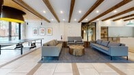 Located at 530 Meeting St in Charleston, South Carolina, this single-story amenity space masterfully combines historic industrial architecture with contemporary design. Exposed brick walls, reclaimed wood accents, and dramatic arched brick openings pay homage to the building's heritage, while modern finishes and abundant natural light from floor-to-ceiling windows create a vibrant, welcoming atmosphere.

The main lounge area features soaring ceilings adorned with rustic wood beams and recessed lighting, anchored by generous seating arrangements including neutral sofas, eclectic armchairs, and a solid wood coffee table. A wall-mounted flat-screen television and ping-pong table add recreational appeal. Warm hardwood and large-format tile floors define distinct zones throughout the space.

A seating nook with reclaimed wood wall cladding, soft carpeting, and a curated gallery of black-and-white artwork provides a cozy, intimate retreat. Mustard-yellow lounge chairs positioned near expansive windows offer street-facing views of the surrounding Charleston neighborhood.

The fully equipped kitchen features sleek white cabinetry, a long quartz island, concrete countertops, full-size appliances, and statement pendant lighting in teal and black — ideal for social gatherings. Throughout, the design balances Charleston's rich architectural history with bold, modern sensibilities, creating an engaging and multifunctional communal environment.
