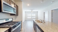 This single-story space offers a clean, contemporary design with a neutral color palette and light hardwood-style flooring throughout the main living areas. The kitchen serves as a central highlight, featuring dark espresso cabinetry that contrasts elegantly with granite countertops. A peninsula with a double basin sink provides additional workspace and a natural division between the kitchen and the adjoining living area. Stainless steel appliances, including a gas range, over-the-range microwave, refrigerator, and dishwasher, complete the well-appointed kitchen.

The living area is bright and open, benefiting from natural light streaming through large windows fitted with horizontal blinds. A ceiling fan overhead adds both functionality and a casual finishing touch to the space.

The bedroom is generously sized with a ceiling fan and access to a walk-in closet equipped with built-in shelving and hanging storage. The bathroom is elegantly finished with marble-style tile flooring and tub surround, a dark-toned vanity with granite countertop and brushed nickel hardware, and a large mirror with overhead lighting, creating a bright and polished atmosphere.