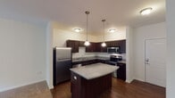 This single-floor residence is designed with functional living in mind, offering a cohesive layout that balances comfort and practicality. The kitchen serves as a standout feature, showcasing rich dark espresso cabinetry, granite countertops, and a full suite of stainless steel appliances, including a refrigerator, range, microwave, and dishwasher. A curved center island provides additional prep space and casual dining potential, while pendant lighting adds a polished finishing touch. Dark hardwood-style flooring runs throughout the kitchen and adjacent areas, lending warmth and visual continuity.

The bedrooms are carpeted for comfort and benefit from natural light through well-placed windows with outdoor greenery views. One bedroom features direct access to a spacious walk-in closet outfitted with wraparound wire shelving, offering generous organizational capacity. A second carpeted bedroom also enjoys natural light and ample space.

The bathroom is clean and straightforward, featuring a dark-cabinetry vanity with a bright mirror, a tub-shower combination, and hardwood-style flooring. Conveniently located off the kitchen, an in-unit laundry area adds everyday practicality. A sliding glass door in one of the main rooms opens to a private balcony, inviting natural light and outdoor views into the living space.