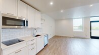 Located at 74 Franklin St in the heart of downtown Buffalo, NY, this thoughtfully designed studio offers a bright, modern living experience with an efficient open-concept layout. Light wood-tone flooring runs throughout the entire space, creating a warm and cohesive aesthetic that complements the crisp white walls and recessed lighting overhead.

The kitchen is well-appointed with white shaker-style cabinetry, brushed gold hardware, a classic white subway tile backsplash, light quartz countertops, and a full suite of stainless steel appliances, including a refrigerator, built-in microwave, dishwasher, and an induction cooktop. Open shelving adds a contemporary touch to the cabinetry layout.

The open living area benefits from a large window that fills the space with natural light and provides views of the surrounding cityscape. A full-height glass entry door further enhances the brightness of the room. A wall-mounted mini-split unit ensures year-round climate comfort.

The bathroom is accessed through a sliding barn door and is finished to a high standard, featuring a frameless glass-enclosed walk-in shower adorned with white subway tile walls, a built-in niche, a mosaic hex-tile floor, and a sleek round mirror above the vanity. The combination of clean lines and quality materials makes this space feel polished and contemporary throughout.