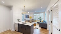 This thoughtfully designed 2-bedroom, 3-bathroom residence makes excellent use of its single-floor layout. The open-concept kitchen and living area serves as the heart of the home, featuring a dark-cabinetry kitchen island with a white quartz countertop, undermount sink, and stainless steel appliances including a dishwasher, refrigerator, and electric range. A striking brass sputnik chandelier adds a stylish focal point above the island. Light wood-tone flooring flows throughout, complementing the crisp white walls and recessed lighting overhead. Large windows in the living area flood the space with natural light and offer views of the surrounding neighborhood, creating an open, airy ambiance. Both bedrooms are comfortably scaled with their own windows providing natural light and urban views. The primary bedroom offers a generous footprint with clean lines and neutral tones. The three bathrooms are finished with modern fixtures, including one featuring terrazzo-style tile flooring, a floating vanity with a black arched mirror, and vertical tile accents, while another showcases a glass-enclosed walk-in shower with mosaic tile flooring and full-height wall tiling. A dedicated utility room and ample cabinetry throughout round out the functional layout of this well-appointed residence.