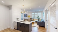 This thoughtfully designed 2-bedroom, 3-bathroom residence makes excellent use of its single-floor layout. The open-concept kitchen and living area serves as the heart of the home, featuring a dark-cabinetry kitchen island with a white quartz countertop, undermount sink, and stainless steel appliances including a dishwasher, refrigerator, and electric range. A striking brass sputnik chandelier adds a stylish focal point above the island. Light wood-tone flooring flows throughout, complementing the crisp white walls and recessed lighting overhead. Large windows in the living area flood the space with natural light and offer views of the surrounding neighborhood, creating an open, airy ambiance. Both bedrooms are comfortably scaled with their own windows providing natural light and urban views. The primary bedroom offers a generous footprint with clean lines and neutral tones. The three bathrooms are finished with modern fixtures, including one featuring terrazzo-style tile flooring, a floating vanity with a black arched mirror, and vertical tile accents, while another showcases a glass-enclosed walk-in shower with mosaic tile flooring and full-height wall tiling. A dedicated utility room and ample cabinetry throughout round out the functional layout of this well-appointed residence.