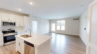 Located at 4705 Windsong Dr in Virginia Beach, VA, this single-floor, 2-bedroom, 2-bathroom residence offers a thoughtfully designed layout with modern finishes throughout. The open-concept kitchen and living area serves as the heart of the home, featuring light hardwood-style flooring, crisp white shaker cabinetry, a central island with a built-in sink and light countertops, white subway tile backsplash, and a full suite of stainless steel appliances including a refrigerator, range, and microwave. Recessed lighting illuminates the kitchen, while large windows and a glass-panel exterior door bathe the living area in natural light. Both bedrooms are carpeted for comfort, with the primary bedroom offering generous proportions and access to a dedicated bathroom. The primary bath includes a double-sink vanity with a large mirror, a soaking tub with shower, and hardwood-style flooring. A second bathroom features a walk-in shower and clean, neutral finishes. Each bedroom benefits from windows with outdoor views, bringing in additional natural light. Two closets provide practical storage throughout the residence. The overall aesthetic is clean, contemporary, and move-in ready.