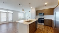 This well-appointed single-floor residence showcases a contemporary design with a seamless open-concept layout connecting the kitchen, dining, and living areas. The kitchen is a standout feature, equipped with stainless steel appliances including a refrigerator, range, and microwave, complemented by rich wood-grain cabinetry, crisp white quartz countertops, and a textured wave-pattern backsplash. A central island with an undermount sink and pendant lighting serves as both a functional workspace and a visual focal point. Warm wood-look flooring runs throughout the main living areas, adding a natural, inviting ambiance, while large windows allow generous natural light to fill the open living space, which also features a ceiling fan. The bedrooms offer plush carpeting, ceiling fans, and windows with outdoor views, providing a comfortable retreat. Both bathrooms are finished with wood-tone vanities, white quartz countertops, and striking large-format marble-look tile in the tub and shower surrounds. The primary bathroom includes a double vanity and a soaking tub, adding a touch of luxury. Overall, the space presents a clean, modern aesthetic with high-quality finishes throughout.