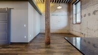 Located at 619 E William St in downtown Wichita, Kansas, this single-floor loft masterfully blends historic industrial character with contemporary finishes. The open living area commands attention with soaring exposed-beam ceilings, original heavy timber columns, and aged brick walls — including a striking arched brick alcove — that speak to the building's rich architectural heritage. Dark hardwood-style flooring grounds the space and complements the raw aesthetic throughout.

The kitchen is a standout feature, outfitted with white cabinetry, dark granite countertops, a central island, stainless steel appliances including a range, microwave, and refrigerator, and a tile backsplash. Pendant lighting and an exposed brick accent wall add warmth and character to the cooking space. Large windows allow natural light to filter in, enhancing the loft's airy atmosphere.

The two bathrooms are finished with modern, textured ceramic tile surrounds wrapping the tub-shower combinations, recessed niche shelving, and wood-look tile flooring — offering a clean contrast to the industrial aesthetic of the main living areas. Two closets and a hallway provide functional storage and circulation throughout. The space also includes an additional unclassified room, adding flexibility for various uses.