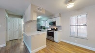This single-floor residence offers a thoughtfully designed layout that balances functionality with modern style. The kitchen is a standout feature, showcasing white shaker-style cabinetry, light quartz countertops, a classic subway tile backsplash, and a full suite of stainless steel appliances including a range, microwave, refrigerator, and dishwasher. A peninsula counter provides additional prep space and serves as a natural divider between the kitchen and the adjacent living area. The living area is bright and welcoming, featuring warm wood-look luxury vinyl plank flooring, neutral-toned walls, and a ceiling fan with integrated lighting. French doors allow natural light to pour in and provide access to the exterior. The bedroom is generously sized with plush carpeting, a ceiling fan, and a window with exterior views, creating a comfortable and restful retreat. The bathroom is clean and well-finished, featuring a white vanity with ample cabinet storage, a large framed mirror, and a shower-tub combination. Consistent wood-look flooring carries through the bathroom and kitchen, tying the interior together with a cohesive, contemporary aesthetic throughout.