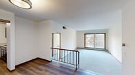 This 2-bedroom, 2-bathroom residence offers a thoughtfully designed layout across a single floor. The entry features a distinctive split-level design, with a hardwood floor landing and a metal-and-wood railing that leads down into the carpeted main living area. The living room is bright and open, with neutral white walls, plush carpet, and a large window that lets in natural light and provides views to the outdoors.

The kitchen is well-equipped with dark cabinetry, light stone countertops, stainless steel appliances including a range, over-the-range microwave, and dishwasher, all set atop durable hardwood-style flooring. A louvered closet door adds a classic touch near the kitchen entry.

The spacious primary bedroom is bathed in natural light from a large window and features plush carpet, baseboard heating, and clean white walls. The second bedroom is equally comfortable, offering soft carpet and an exterior-facing window. Both bathrooms are finished with tile flooring; one features a full tub-shower combo with large-format stone-look tile surround and chrome fixtures. A dedicated closet provides additional storage. The overall ambiance is clean, functional, and move-in ready.