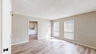 This efficiently designed single-floor unit offers a thoughtful layout across a cozy footprint, comprising a living room, kitchen, bathroom, hallway, and three closets. The living room is a bright, open space finished with light wood-look vinyl plank flooring and neutral beige walls. A textured popcorn ceiling adds character, while multiple windows fitted with horizontal blinds allow generous natural light to fill the room. A door provides direct exterior access, enhancing the sense of openness. The kitchen is positioned adjacent to the living area and features white raised-panel cabinetry extending from floor to ceiling, light stone-look countertops, a stainless steel double-basin sink, and a white dishwasher. The layout is clean and functional, offering ample storage for a unit of this scale. The bathroom is finished with a white vanity and cabinetry, a light speckled countertop, an undermount sink, and a wall-mounted mirror, creating a tidy and practical space. Consistent light wood-look flooring runs throughout the unit, unifying the spaces and contributing to the overall bright, neutral palette. Three closets provide notable storage capacity. The unit presents a clean, move-in-ready aesthetic with a simple, cohesive design throughout.