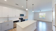 Located at 820 Clawson Pl in Fort Mill, SC, this single-floor, one-bedroom, one-bathroom residence offers a thoughtfully designed layout with modern finishes throughout. The open-concept kitchen and living area serves as the heart of the unit, showcasing white upper cabinetry, gray lower cabinets, white quartz countertops, and a classic subway tile backsplash. A central kitchen island provides additional prep and seating space, illuminated by stylish pendant lighting. Stainless steel appliances, including a refrigerator, range, microwave, and dishwasher, complete the kitchen. Light hardwood flooring flows seamlessly throughout the entire unit, enhancing the bright, cohesive aesthetic. The living area benefits from large windows and a glass-paneled exterior door that allow abundant natural light and outdoor views, complemented by a ceiling fan overhead. The bedroom is a comfortable, well-proportioned space with its own ceiling fan, a generous window with outdoor views, and access to a dedicated closet. The full bathroom features a gray vanity with a white sink, a tub-shower combination with tile surround, and clean, minimalist finishes. The overall ambiance is fresh, modern, and move-in ready.