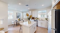 This well-appointed two-story home offers a thoughtfully designed layout spread across two floors, connected by a carpeted staircase with clean white textured walls. The main level showcases an open-concept kitchen and dining area, where bright white shaker cabinetry, quartz countertops, and a central island with bar seating take center stage. Stainless steel appliances, a built-in dishwasher, and recessed lighting complete the kitchen's modern aesthetic. Light wood-tone flooring flows throughout the main living areas, adding warmth and continuity. The dining area features a sliding glass door that opens to a private balcony, offering views of the surrounding neighborhood and filling the space with natural light. Upstairs, a versatile loft area with light wood flooring and a ceiling fan provides an ideal lounge or home office space. The bedrooms are carpeted and serene, each featuring ceiling fans, generous closet space, and large windows that invite natural light. A well-finished bathroom includes a dual-sink vanity with white cabinetry, quartz counters, and a glass-enclosed shower. The attached garage features an automatic door opener and offers ample storage and parking space, completing this functional and stylish home.