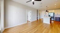 Located at 2307 N Tryon St in Charlotte's vibrant NoDa neighborhood, this single-floor condo offers 910 square feet of thoughtfully designed living space with 2 bedrooms and 3 bathrooms. The open-concept layout connects the kitchen and living room, creating a seamless flow ideal for everyday living and entertaining. Light hardwood flooring extends throughout the main living area, complemented by neutral gray walls and crisp white trim that give the interior a clean, contemporary feel. A ceiling fan anchors the living space, contributing to both comfort and airflow. Built-in shelving is visible along one wall, offering practical storage within the living area. The kitchen features dark pendant lighting and light-colored countertops, adding a modern contrast to the bright surroundings. The primary bedroom spans 170 square feet, providing a comfortable private retreat. Two dedicated closets offer organized storage throughout the unit. An in-unit laundry room adds everyday convenience. With three full bathrooms serving two bedrooms, the layout is well-suited for roommates or guests. The overall ambiance is modern, light-filled, and functional.