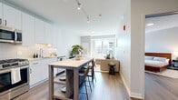 Located at 7215 N District Ave in Lincolnwood, IL, this well-designed one-bedroom, one-bathroom residence offers a thoughtfully arranged open-concept floor plan that maximizes every square foot. Wood-look flooring flows consistently throughout, complemented by a neutral, light gray color palette that creates a clean, modern aesthetic.

The kitchen is outfitted with crisp white cabinetry, white quartz countertops, a subway tile backsplash, stainless steel appliances including a gas range, microwave, and full-size refrigerator, and track lighting overhead. A freestanding kitchen island with bar seating serves as a functional dining and gathering space.

The living room benefits from large windows that draw in generous natural light and provide views of the surrounding neighborhood. The space comfortably accommodates a sectional sofa and media setup, maintaining an airy, open feel.

The spacious primary bedroom features room for a full bedroom suite, with access to a dedicated closet. The bathroom is finished with a white vanity, LED-backlit mirror, subway tile tub-surround, and wood-look flooring that ties the space together cohesively.

The overall ambiance is contemporary and functional, with consistent modern finishes throughout.