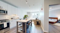 Located at 7215 N District Ave in Lincolnwood, IL, this well-designed one-bedroom, one-bathroom residence offers a thoughtfully arranged open-concept floor plan that maximizes every square foot. Wood-look flooring flows consistently throughout, complemented by a neutral, light gray color palette that creates a clean, modern aesthetic.

The kitchen is outfitted with crisp white cabinetry, white quartz countertops, a subway tile backsplash, stainless steel appliances including a gas range, microwave, and full-size refrigerator, and track lighting overhead. A freestanding kitchen island with bar seating serves as a functional dining and gathering space.

The living room benefits from large windows that draw in generous natural light and provide views of the surrounding neighborhood. The space comfortably accommodates a sectional sofa and media setup, maintaining an airy, open feel.

The spacious primary bedroom features room for a full bedroom suite, with access to a dedicated closet. The bathroom is finished with a white vanity, LED-backlit mirror, subway tile tub-surround, and wood-look flooring that ties the space together cohesively.

The overall ambiance is contemporary and functional, with consistent modern finishes throughout.