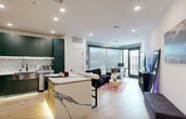 This efficiently designed 550-square-foot, single-story unit on Miss Gulch offers a thoughtfully arranged 1-bedroom, 1-bathroom floor plan. The open-concept kitchen and living area serves as the heart of the home, featuring deep forest-green flat-front cabinetry, a striking herringbone-patterned tile backsplash, stainless steel appliances, and a waterfall-edge marble-look island with bar seating. Light wood-tone flooring and recessed lighting tie the space together seamlessly. The living area offers large floor-to-ceiling windows with roller shades, flooding the space with natural light and providing outdoor views, while also accommodating a dedicated workspace area. The 120-square-foot primary bedroom features carpet flooring, a large window with roller shades, balcony access, and a pendant light fixture. The bathroom makes a bold design statement with a striking black-and-white geometric tile floor, a dark wood floating vanity with gold hardware accents, an oversized mirror, and contemporary vanity lighting. Throughout the unit, clean white walls, modern door hardware, and a cohesive monochromatic accent palette create a polished, contemporary ambiance suited for urban living.