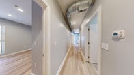 Located at 770 Grant St in Denver's Capitol Hill neighborhood, this two-bedroom, three-bathroom unit showcases a striking blend of industrial character and modern finishes. The expansive living room immediately impresses with soaring ceilings that reveal exposed steel trusses, red structural beams, and visible ductwork, all bathed in natural light streaming through large windows fitted with vertical blinds. A decorative wire-cage chandelier adds an artful focal point to this bright, open space, finished with light hardwood-style flooring found throughout. The kitchen features crisp white cabinetry, a mosaic tile backsplash in rich blues and greens, light stone countertops, and white appliances including a dishwasher, range, microwave, and refrigerator. A long hallway with exposed overhead ductwork connects the living areas to the private quarters. Both bedrooms offer a calm, neutral palette with natural light and ample closet space, including mirrored sliding-door closets. The three bathrooms are clean and functional, featuring modern vanities with mirrored medicine cabinets and mosaic tile accents, with one bathroom offering a full tub/shower combo. A dedicated laundry room with washer and dryer completes this well-appointed urban home.