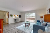 Located at 8570 Jamestown Dr in Winter Haven, Florida, this single-story residence offers a thoughtfully designed layout that balances comfort and functionality throughout. The living room serves as the heart of the home, featuring wood-look flooring, neutral walls, and a large sliding glass door fitted with vertical blinds that opens to a private outdoor patio, allowing an abundance of natural light to fill the space. A pass-through window connects the living area to the kitchen, adding an open, communicative feel between rooms. The kitchen is appointed with warm honey-toned wood cabinetry, white countertops, a double-basin sink beneath a window, and includes a dishwasher and refrigerator. Adjacent to the kitchen, a dedicated dining area features wood-look flooring and a ceiling light fixture, providing an intimate setting for meals. The bedroom is generously sized with plush carpeting, a natural light-welcoming window, and ample room for large furniture. The home includes two bathrooms, each finished with wood-look flooring, white vanities with wide mirrors, and tub-shower combinations, presenting a clean and practical design. Overall, the space carries a bright, welcoming ambiance suited for comfortable everyday living in Central Florida.