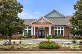 This 1,020-square-foot single-floor residence at 4000 Penuche Way in Holly Springs, NC features 2 bedrooms and 2 bathrooms across a thoughtfully designed open layout. The combined kitchen and living area serves as the heart of the home, with warm-toned luxury vinyl plank flooring, crown molding, and ceiling fans throughout. The kitchen is equipped with cream cabinetry, granite countertops, stainless steel appliances including a side-by-side refrigerator, electric range, and over-the-range microwave, plus a central island with pendant lighting and a built-in sink. The living area flows seamlessly from the kitchen, featuring natural light from windows with blinds. The primary bedroom spans 170 square feet and is served by an en-suite bathroom with a dual-sink vanity, ample cabinetry, and a walk-in glass shower. The second bedroom features plush carpeting, a ceiling fan, and a window with outdoor views. The second bathroom includes a full tub/shower combo and a single-sink vanity. A dedicated laundry room houses full-size washer and dryer units with upper storage cabinets. Two closets and two hallways complete this well-appointed home.