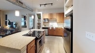 This thoughtfully designed two-bedroom, two-bathroom residence offers a comfortable and functional single-floor layout. The open kitchen is a standout feature, showcasing warm wood cabinetry, granite countertops, a stainless steel appliance suite including a refrigerator, range with cooktop island, and dishwasher, complemented by a classic tile backsplash, built-in open shelving, and polished concrete-style flooring. Track lighting and an exposed duct detail add an urban, industrial touch to the space.

The living area features light flooring, large windows with blinds that allow ample natural light, and access to an outdoor area through a glass door. Both bedrooms are carpeted and generously sized, each with multiple windows offering views of surrounding greenery. The bedrooms feature neutral wall tones, ceiling fans, and ample room for storage.

Each bathroom is well-appointed with wood-toned cabinetry, granite countertops, large vanity mirrors, and tile flooring. One bathroom includes a soaking tub and tiled shower combination, while the other features a glass-enclosed walk-in shower, offering distinct options for relaxation and convenience.