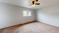 Located at 1708 E Main St in Kent, Ohio, this one-bedroom, one-bathroom unit offers a practical and straightforward layout across a single floor. The main living area features neutral gray walls and plush carpeting, creating a clean and simple environment. A central dividing wall separates the entry from the kitchen area, which includes hardwood-style flooring and a full-size refrigerator. The bedroom is generously sized relative to the overall footprint, finished with soft carpet, light gray walls, and a ceiling fan with integrated lighting. A window allows natural light to filter in, and a wall-mounted air conditioning unit provides climate control alongside baseboard heating. The bathroom is well-appointed with hardwood-style flooring, a full tub and shower combo, a toilet, and a wood-toned vanity with a white countertop. Throughout the unit, white trim and neutral tones contribute to a cohesive, understated aesthetic. The layout is efficient, making practical use of every area, and the unit is well-suited for those seeking a straightforward, low-maintenance living space in Kent, Ohio.