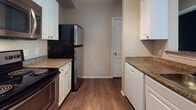 This well-appointed single-floor residence offers a thoughtfully designed layout that balances modern finishes with comfortable living spaces. The galley-style kitchen is a standout feature, showcasing rich dark cabinetry paired with light quartz countertops and a full suite of stainless steel appliances, including a refrigerator, electric range, and over-the-range microwave. Warm hardwood-style flooring runs throughout the kitchen and main living areas, complemented by track lighting overhead that adds both function and contemporary style. Crown molding details carry throughout the unit, lending an elevated sense of refinement. The open living area flows naturally from the kitchen, providing a versatile space filled with clean lines and neutral tones. The bedrooms are carpeted for comfort and feature large windows dressed with horizontal blinds, allowing ample natural light and views of surrounding greenery. Built-in shelving in one bedroom offers practical storage and display space. The bathroom is finished with a quartz vanity countertop, an undermount sink, brushed nickel fixtures, and a walk-in shower. Throughout the space, neutral wall colors, consistent finishes, and a clean, modern aesthetic create a cohesive and inviting environment.